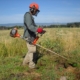 Photo représentant l'activité d'entretien d'espaces verts d'OASURE. On observe un salarié en train de débroussailler un terrain avec une débroussailleuse.
