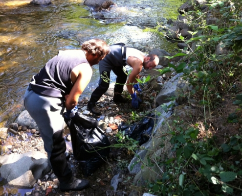 Photo représentant l'activité d'entretien d'espaces verts. On observe des salariés au bord d'une rivière en train de désherber manuellement.