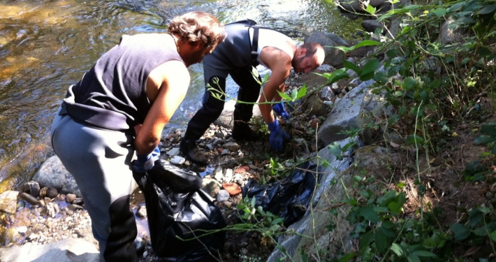 Photo représentant l'activité d'entretien d'espaces verts. On observe des salariés au bord d'une rivière en train de désherber manuellement.