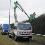 Photo représentant l'activité d'entretien des espaces verts d'OASURE. On observe un salarié suspendu sur une nacelle pour tailler le haut d'une grande haie.