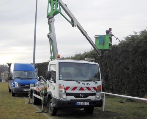 Photo représentant l'activité d'entretien des espaces verts d'OASURE. On observe un salarié suspendu sur une nacelle pour tailler le haut d'une grande haie.