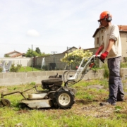 Photo représentant une ancienne activité d'OASURE de service à la personne. Elle est illustré par un salarié en train de passé le motoculteur dans un jardin.