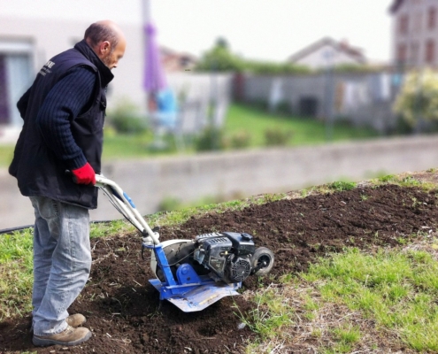 Photo représentant une ancienne activité d'OASURE de service à la personne. Elle est illustré par un salarié en train de passé le motoculteur dans un jardin.