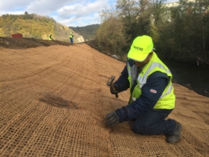 Un salarié d'OASURE fixe du treillis coco sur une berge de rivière à l'aide d'agrafe.