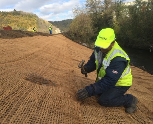 Un salarié d'OASURE fixe du treillis coco sur une berge de rivière à l'aide d'agrafe.